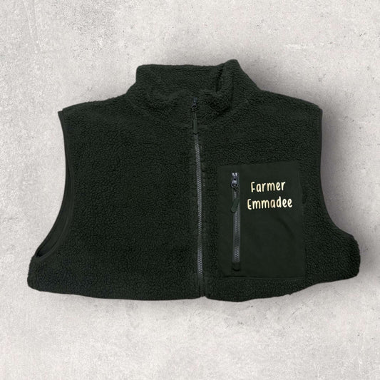 Black fleece gilet with 'Farmer Emmadee' text on a light gray background