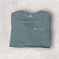Folded teal t-shirt with 'dog mama' text on a light gray surface