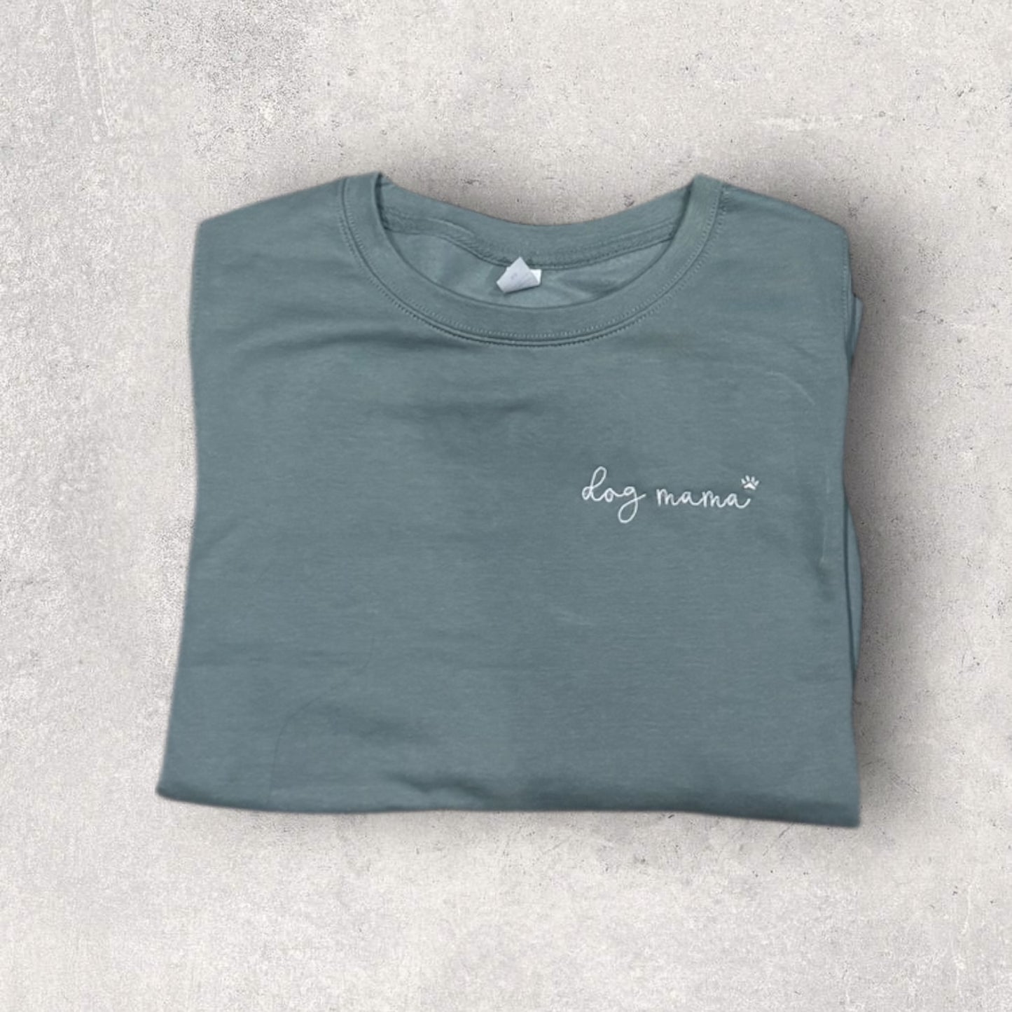 Folded teal t-shirt with 'dog mama' text on a light gray surface