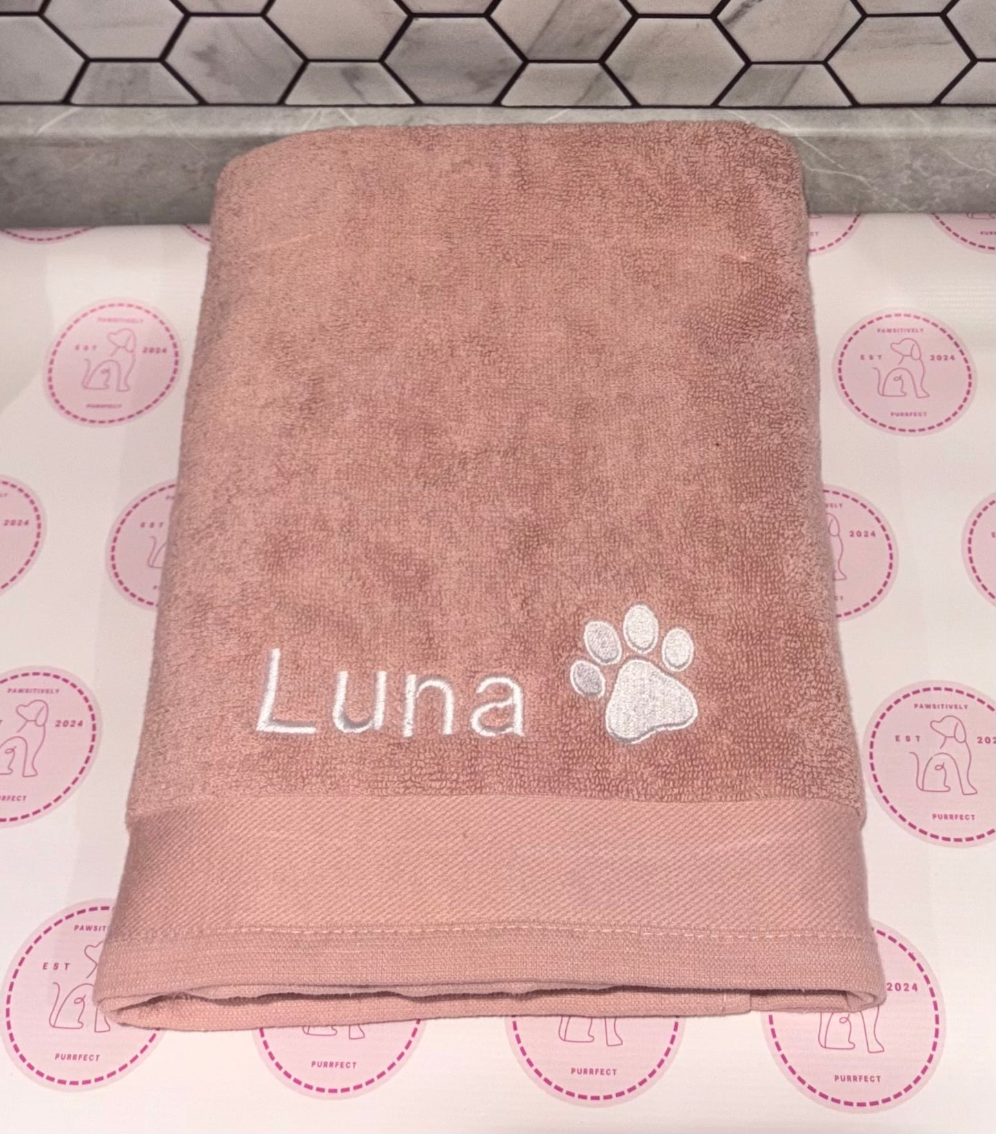 Brown towel with 'Luna' and a paw print on a patterned background