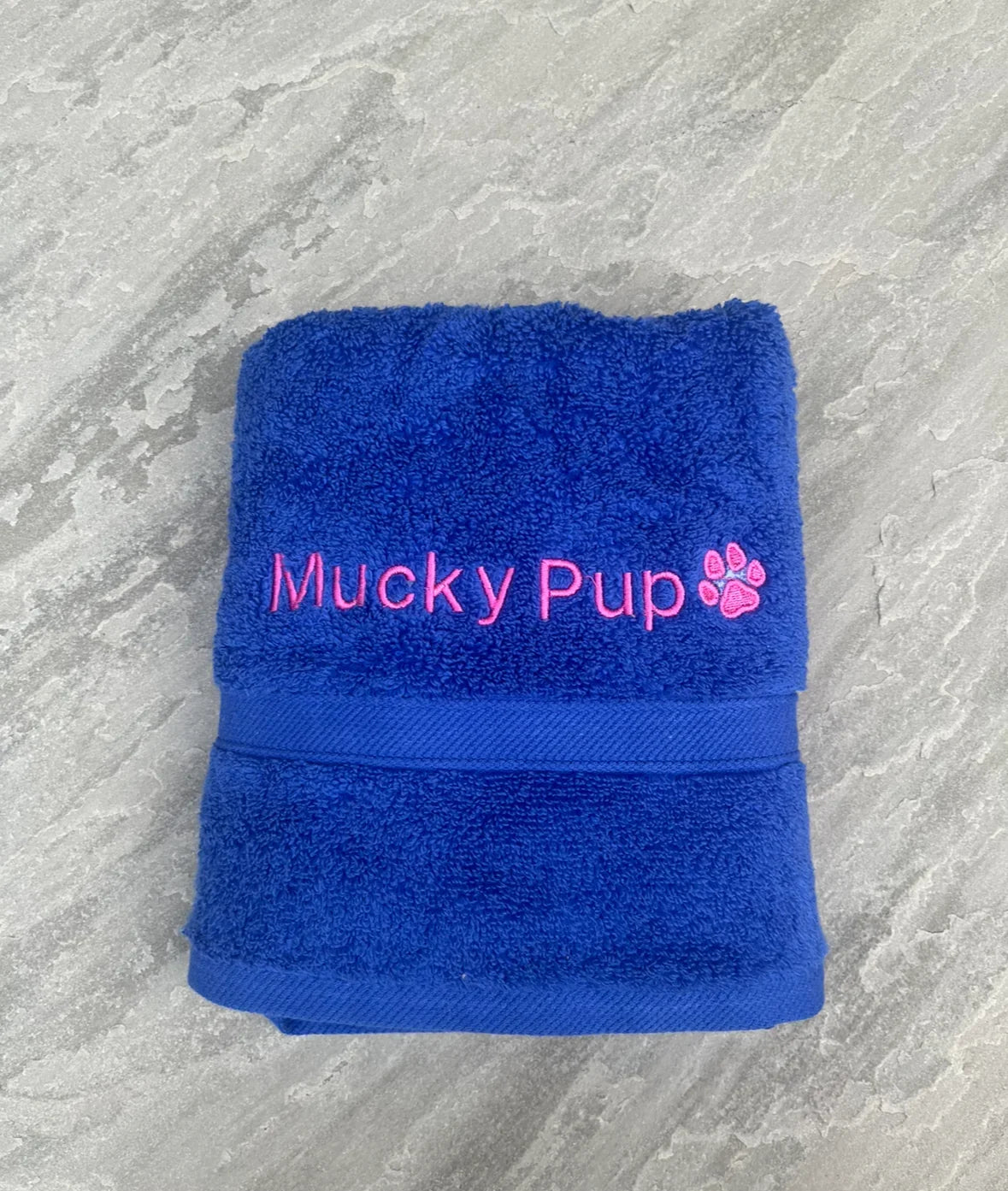 Blue towel with 'Mucky Pup' embroidery on a gray surface