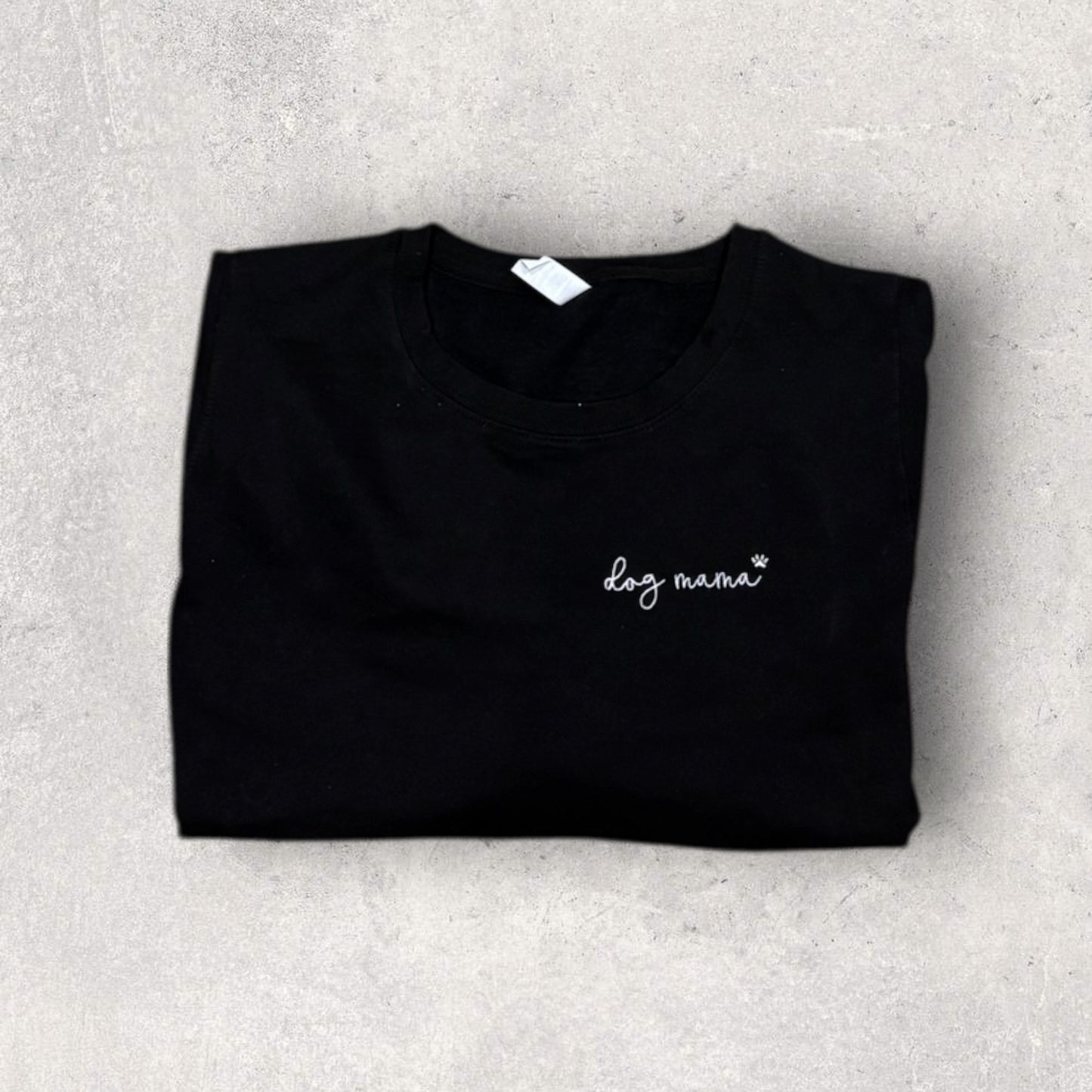 Folded black shirt with 'dog mama' text on a gray surface