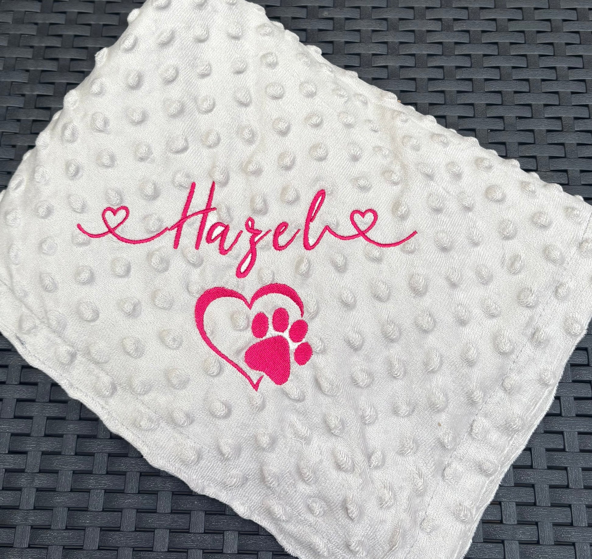 light grey textured blanket with pink text and heart design on a dark woven surface