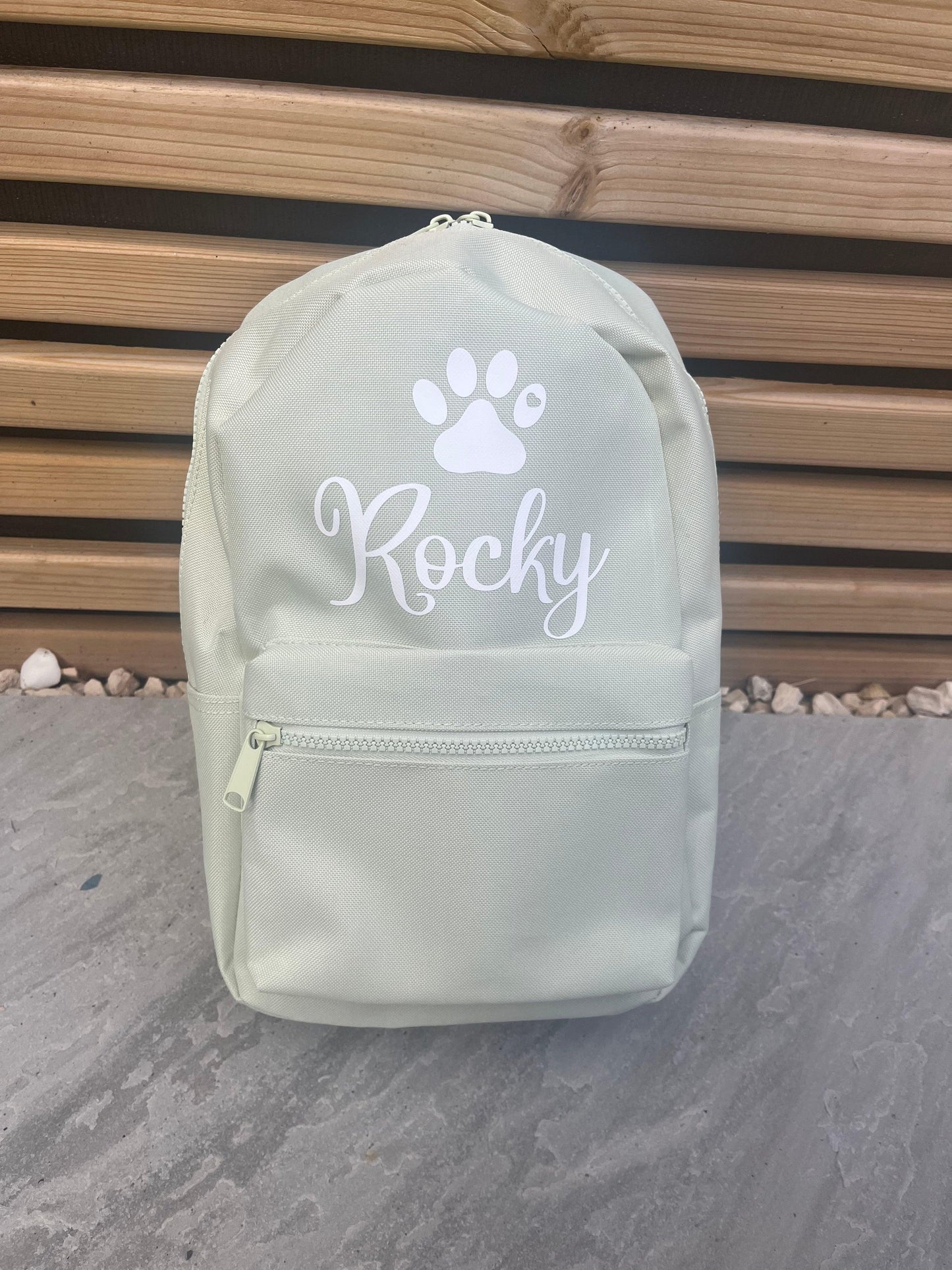Light green backpack with 'Rocky' and a paw print on a wooden background