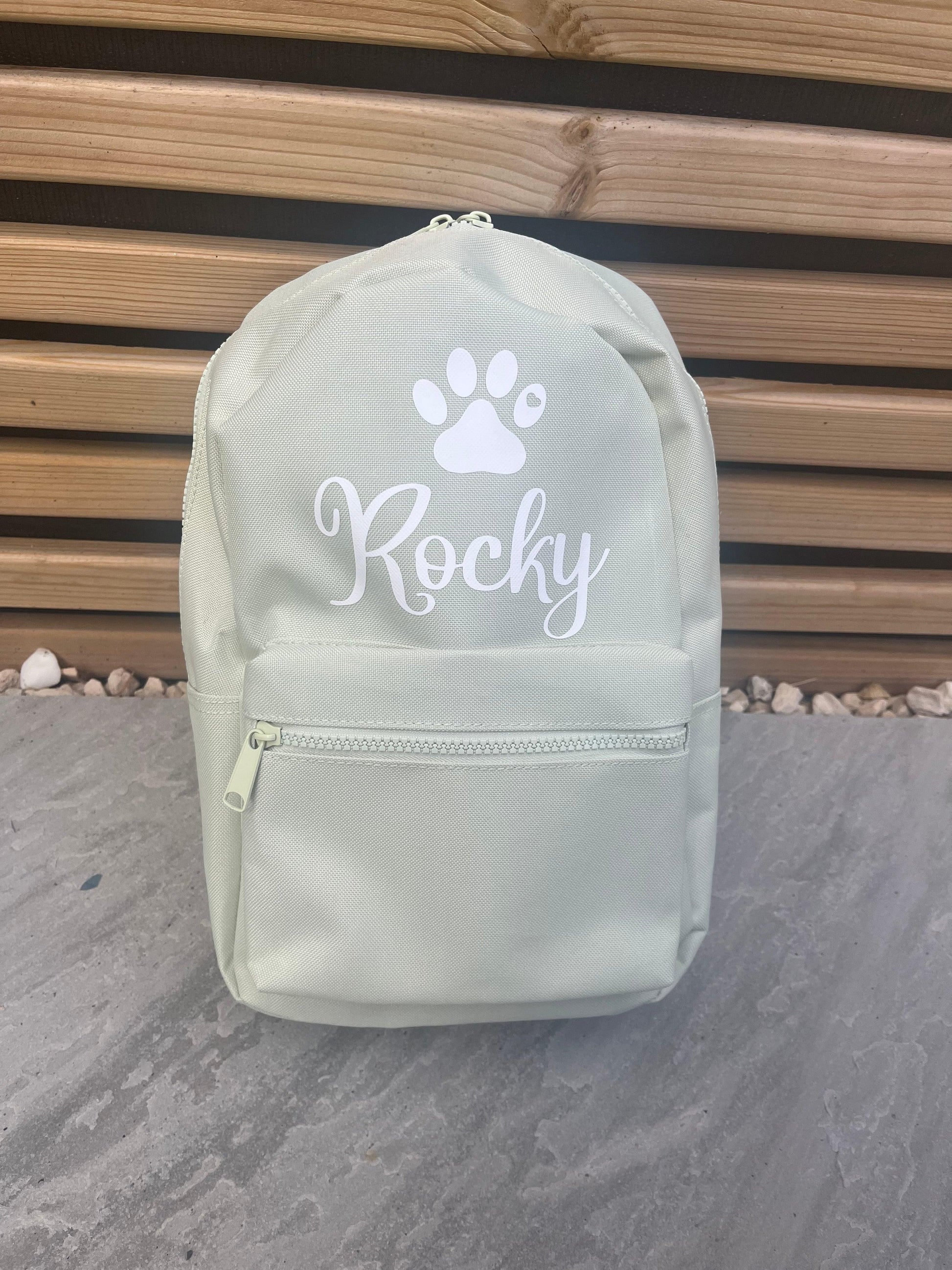 Light green backpack with 'Rocky' and a paw print on a wooden background