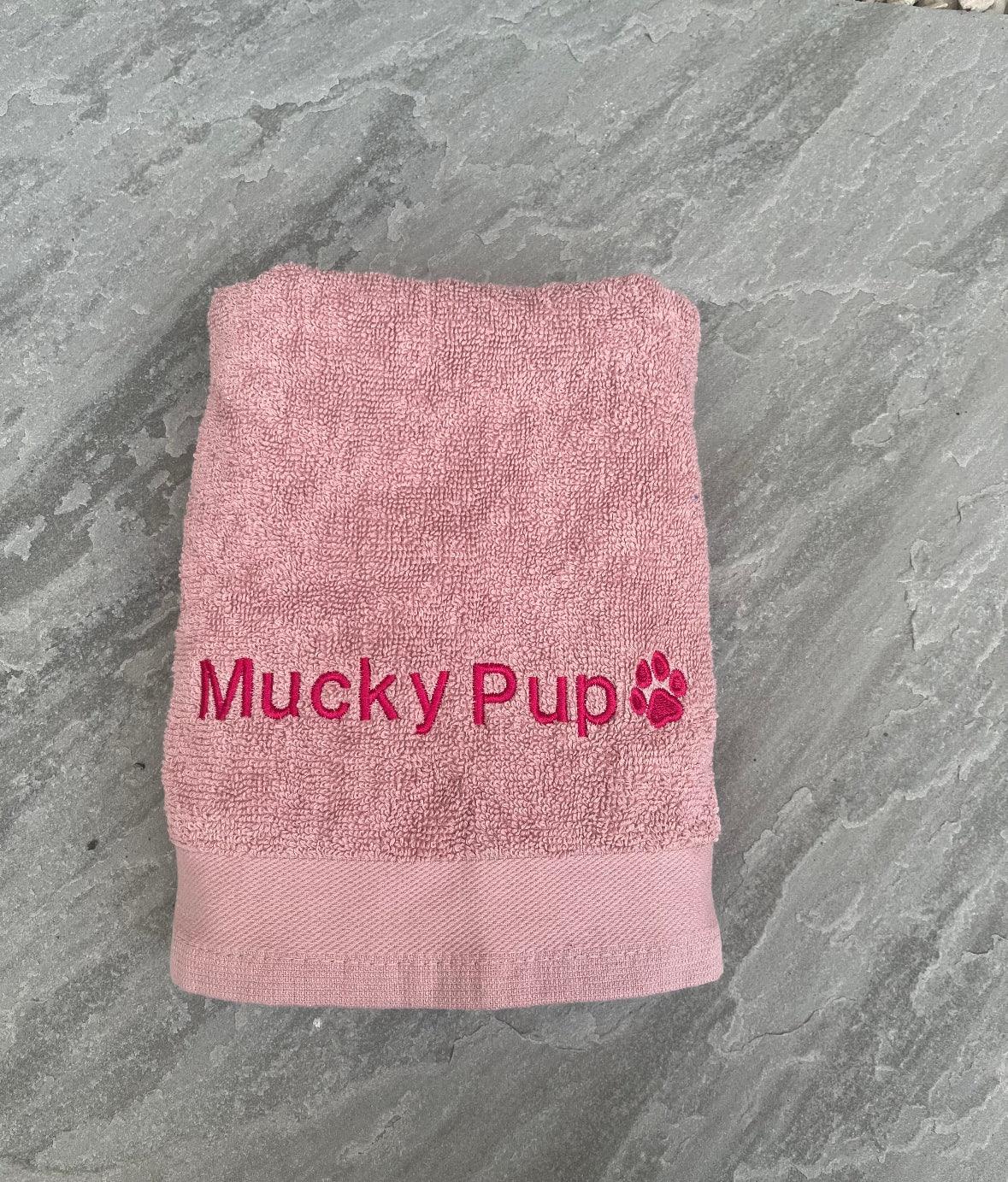 Pink towel with 'Mucky Pup' text on a gray stone surface