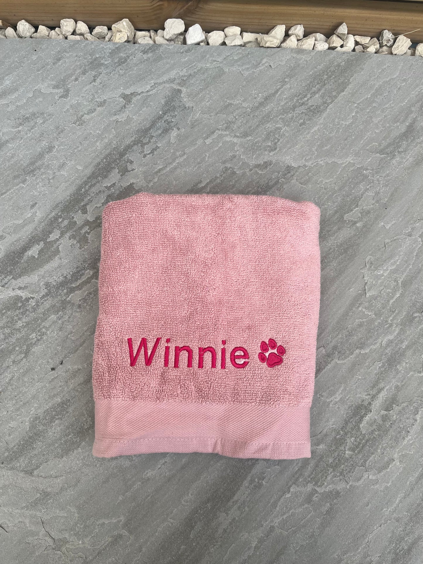 Pink towel with 'Winnie' and a paw print on a stone surface