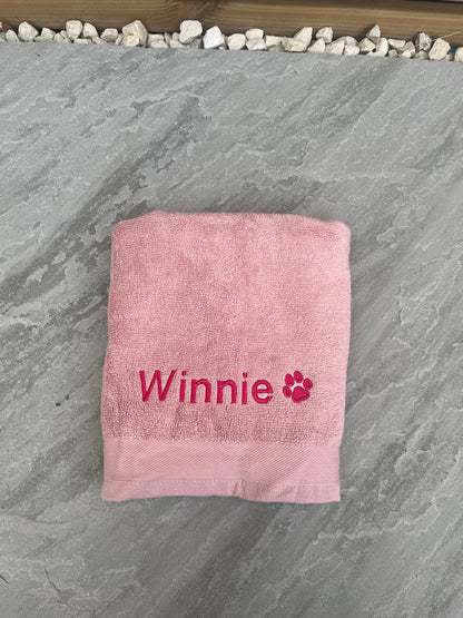 Pink towel with 'Winnie' and a paw print on a stone surface