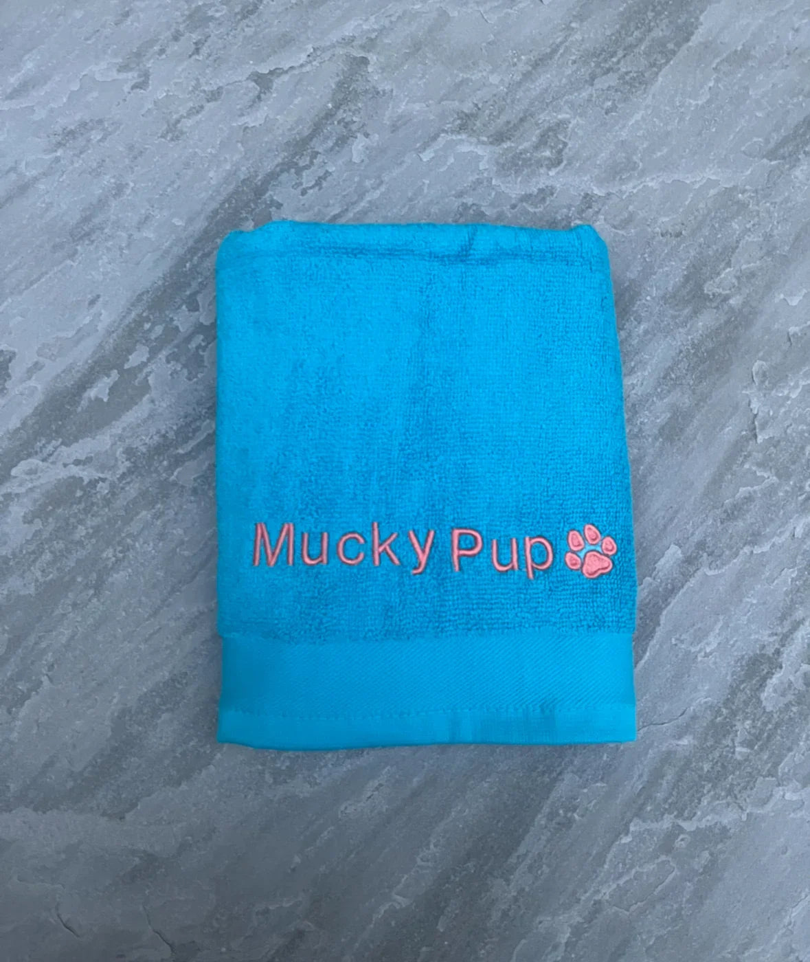 Blue towel with 'Mucky Pup' logo on a gray marble background