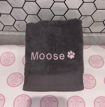 Gray towel with 'Moose' and paw print on a tiled bathroom floor