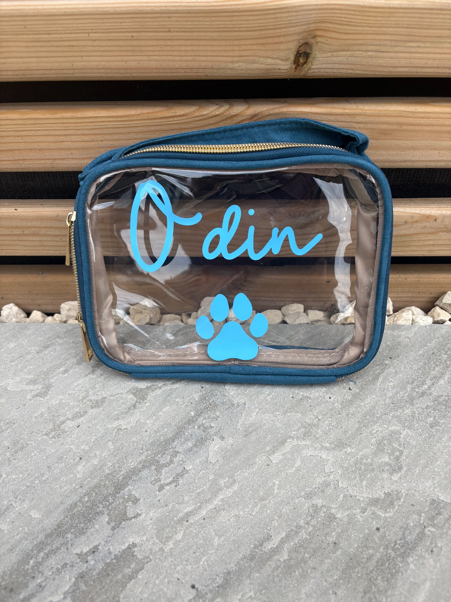 Clear vanity bag with blue text and paw print on a wooden and stone surface