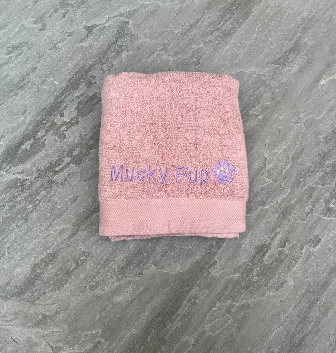Pink towel with 'Mucky Pup' branding on a gray surface