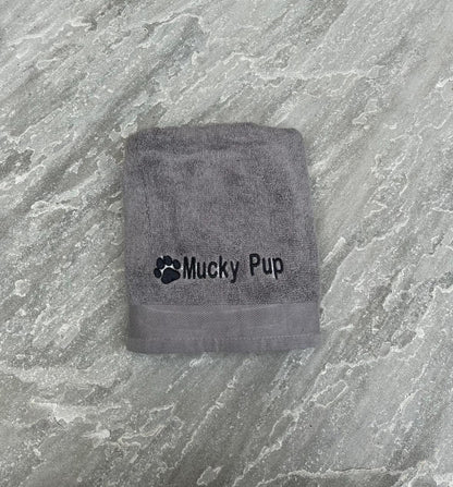 Gray towel with 'Mucky Pup' branding on a textured gray surface