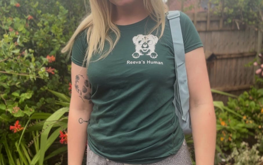 Person wearing a green t-shirt with a logo and text, standing outdoors with plants in the background