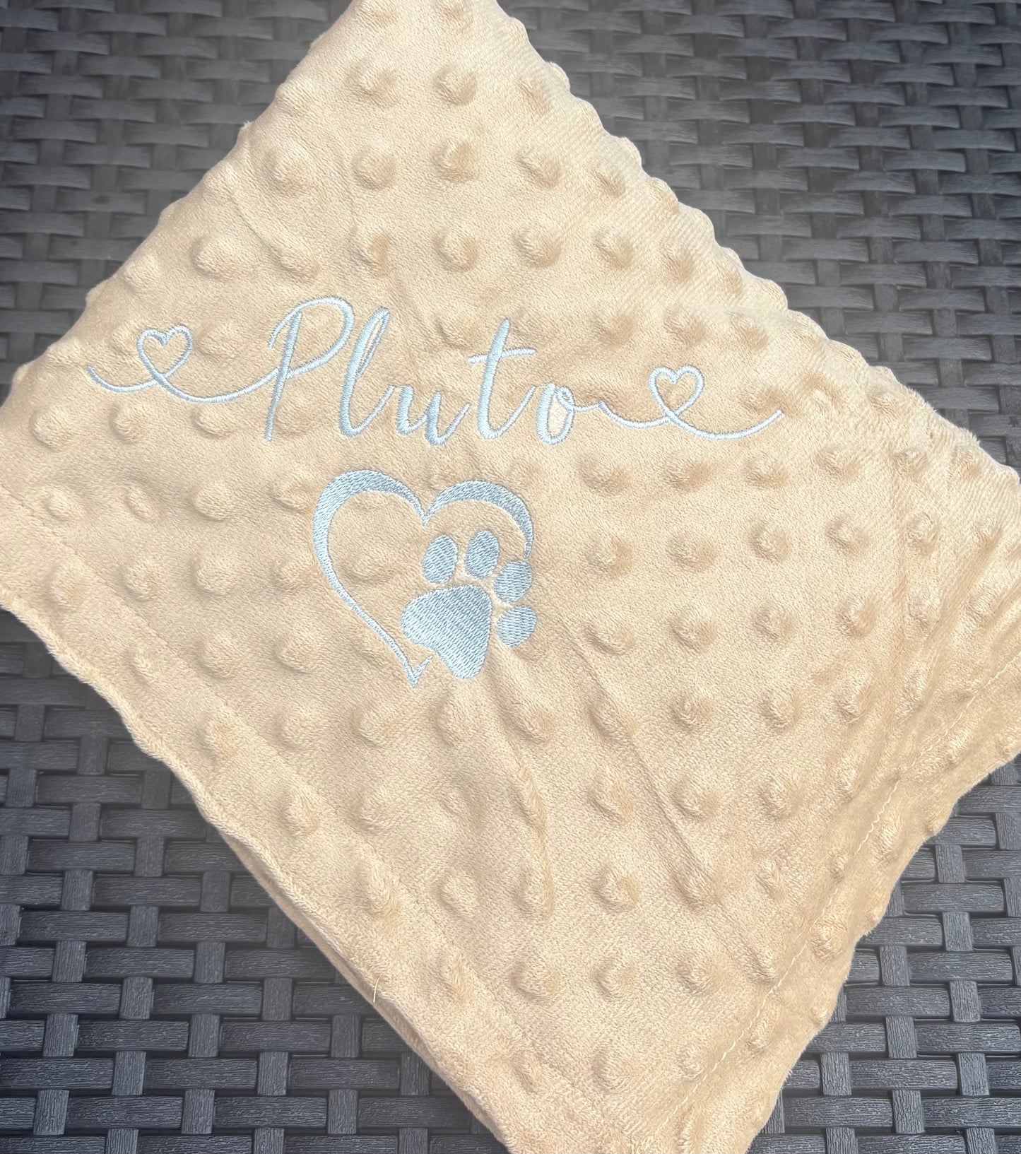 Beige textured blanket with 'Pluto' and a paw print on a dark woven surface