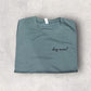 Folded teal t-shirt with 'dog mama' text on a light gray surface