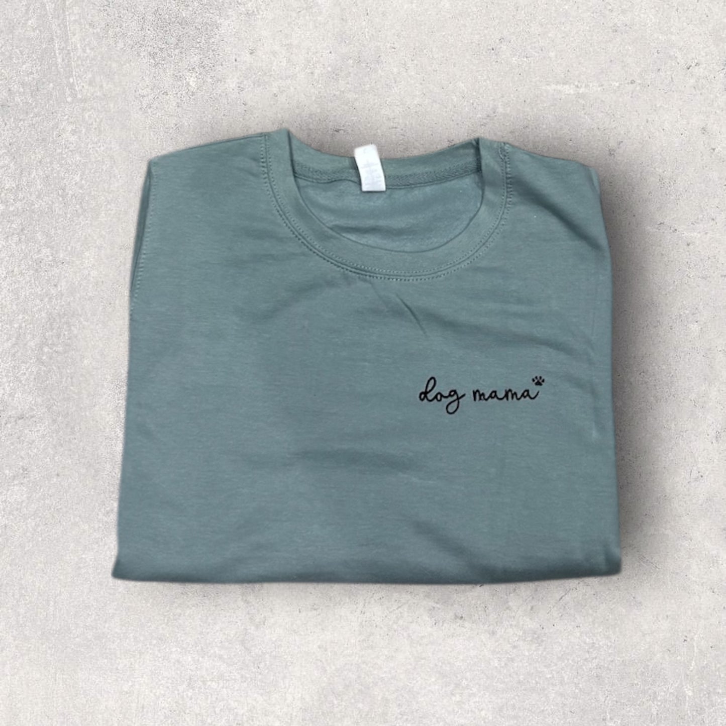 Folded teal t-shirt with 'dog mama' text on a light gray surface
