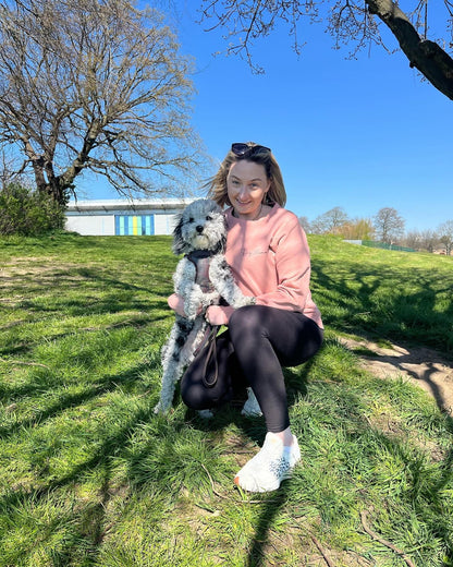 Woman sitting on grass with a dog, wearing a pink sweater and sunglasses.