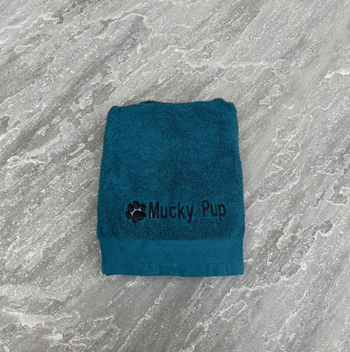 Teal towel with 'Mucky Pup' logo on a gray marble surface