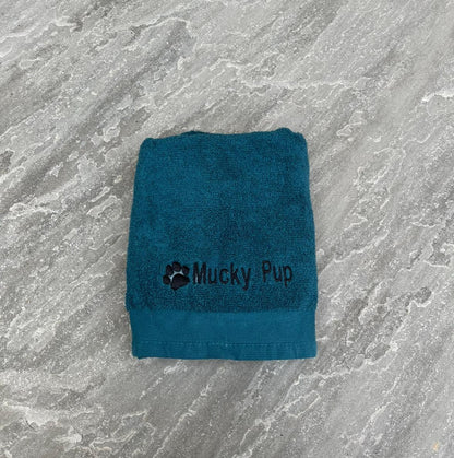Teal towel with 'Mucky Pup' logo on a gray marble surface
