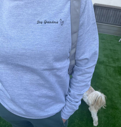 Person wearing a light blue sweatshirt with 'Dog Grandma' text, standing on grass with a dog.