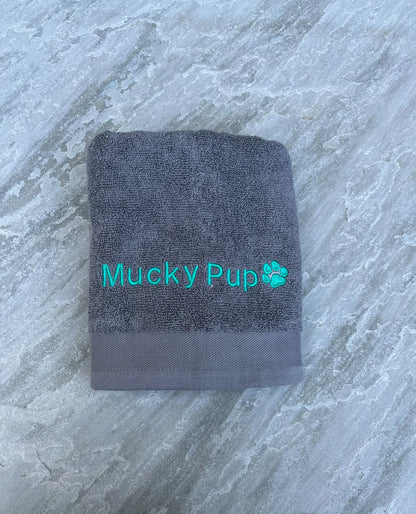 Gray towel with 'Mucky Pup' embroidery on a marble surface