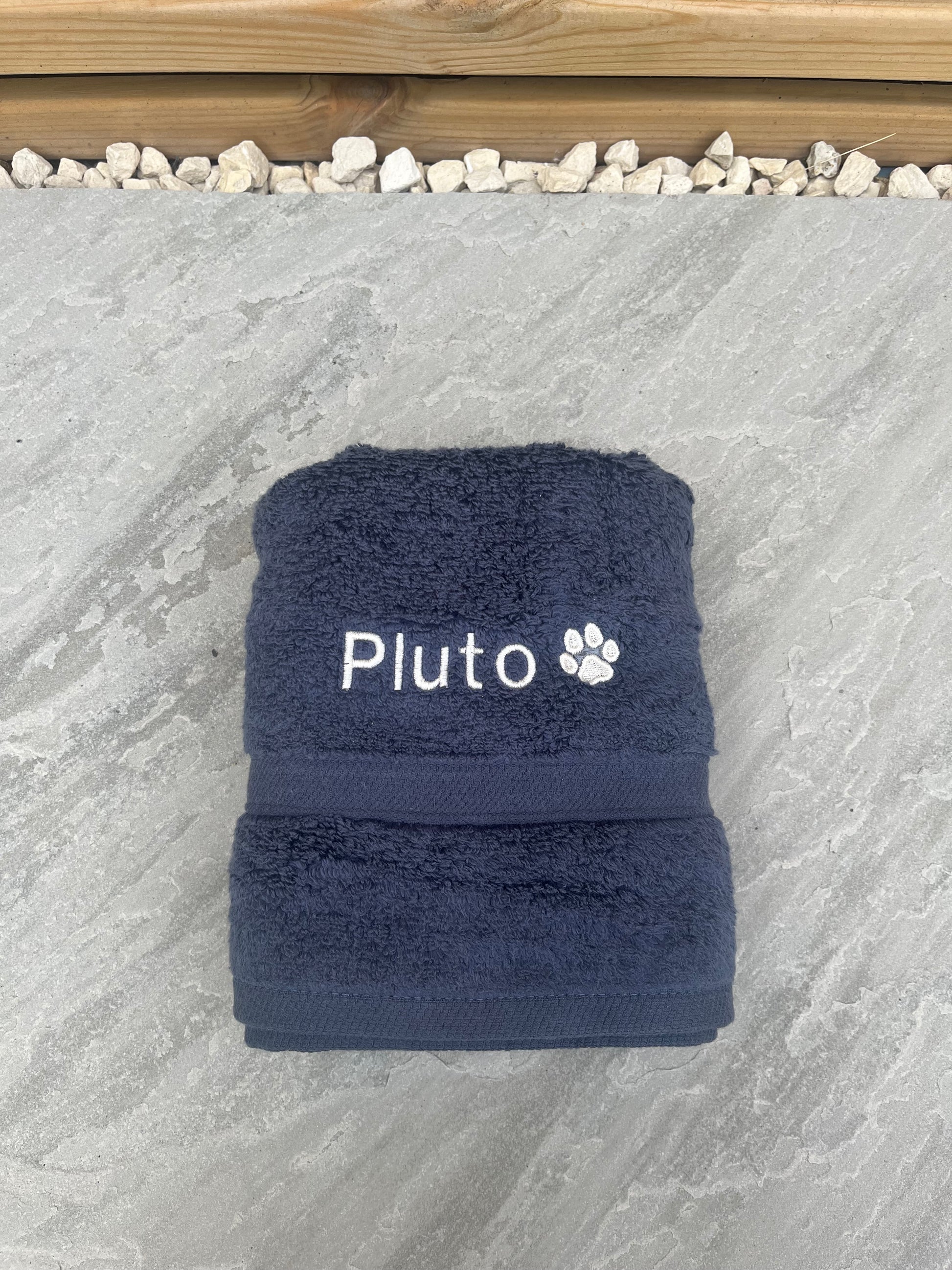 Navy blue towel with 'Pluto' embroidered on a stone surface