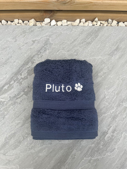 Navy blue towel with 'Pluto' embroidered on a stone surface