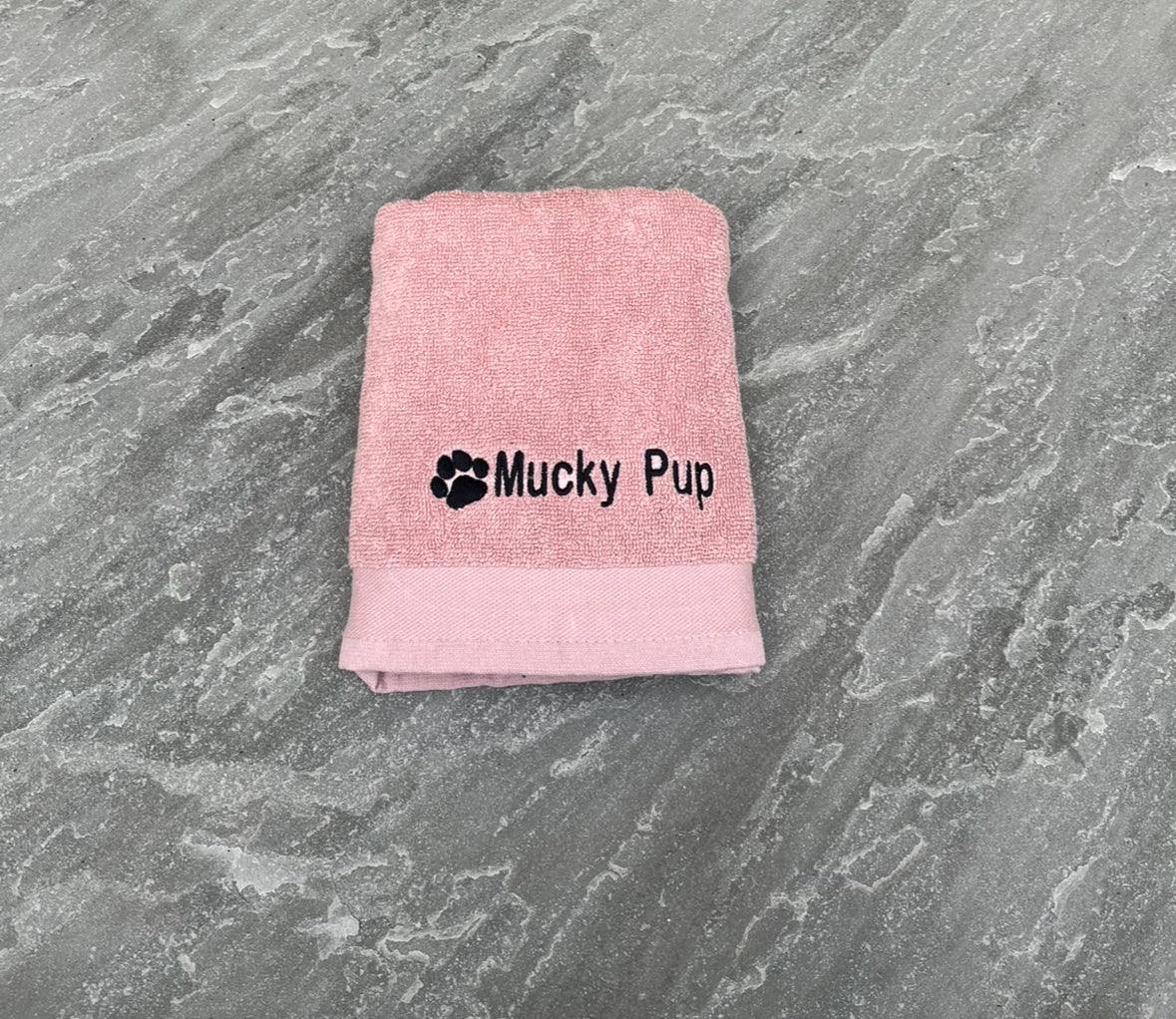 Pink towel with 'Mucky Pup' text on a gray surface