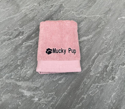 Pink towel with 'Mucky Pup' text on a gray surface