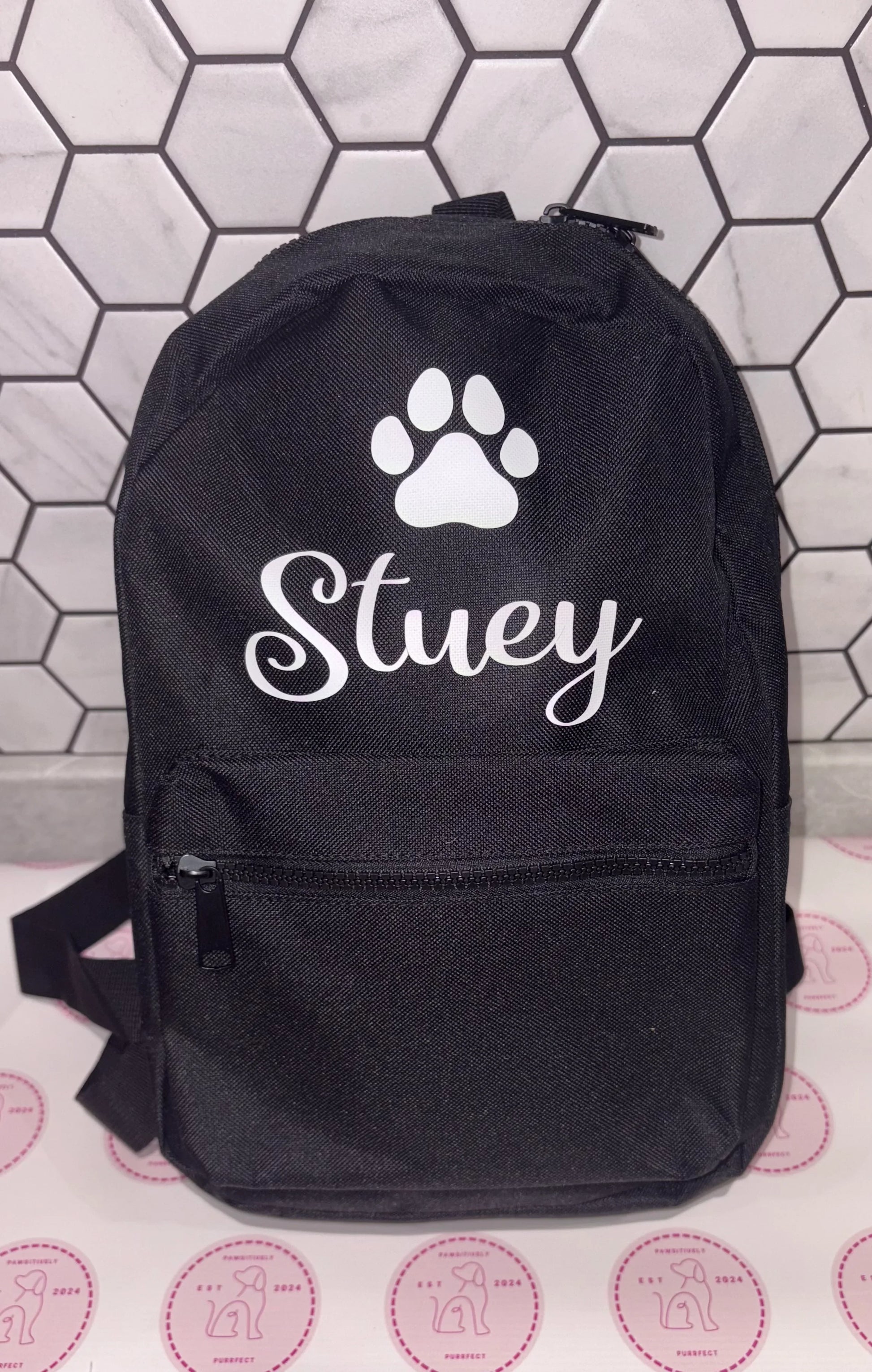 Black backpack with a paw print and 'Stuey' text on a tiled background