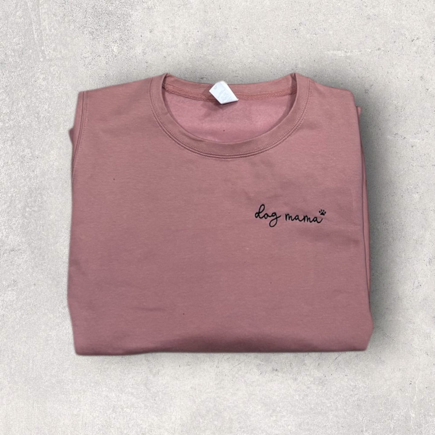 Folded mauve t-shirt with 'dog mama' text on a light gray surface