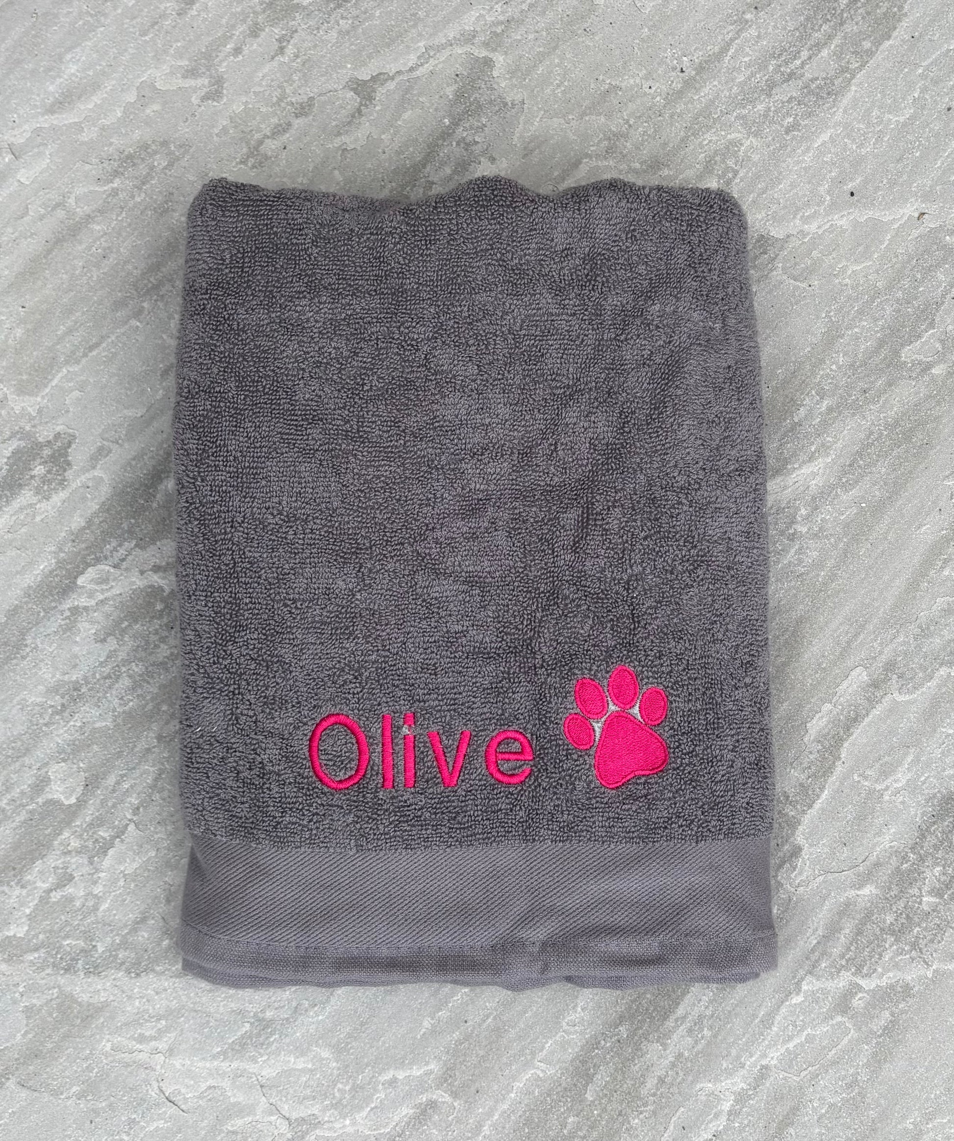 Gray towel with 'Olive' and a paw print in pink on a textured gray background