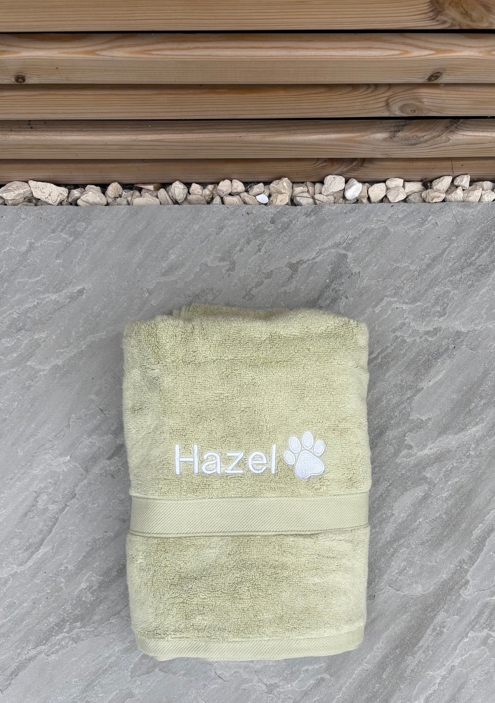 Green towel with 'Hazel' and a paw print on a stone surface