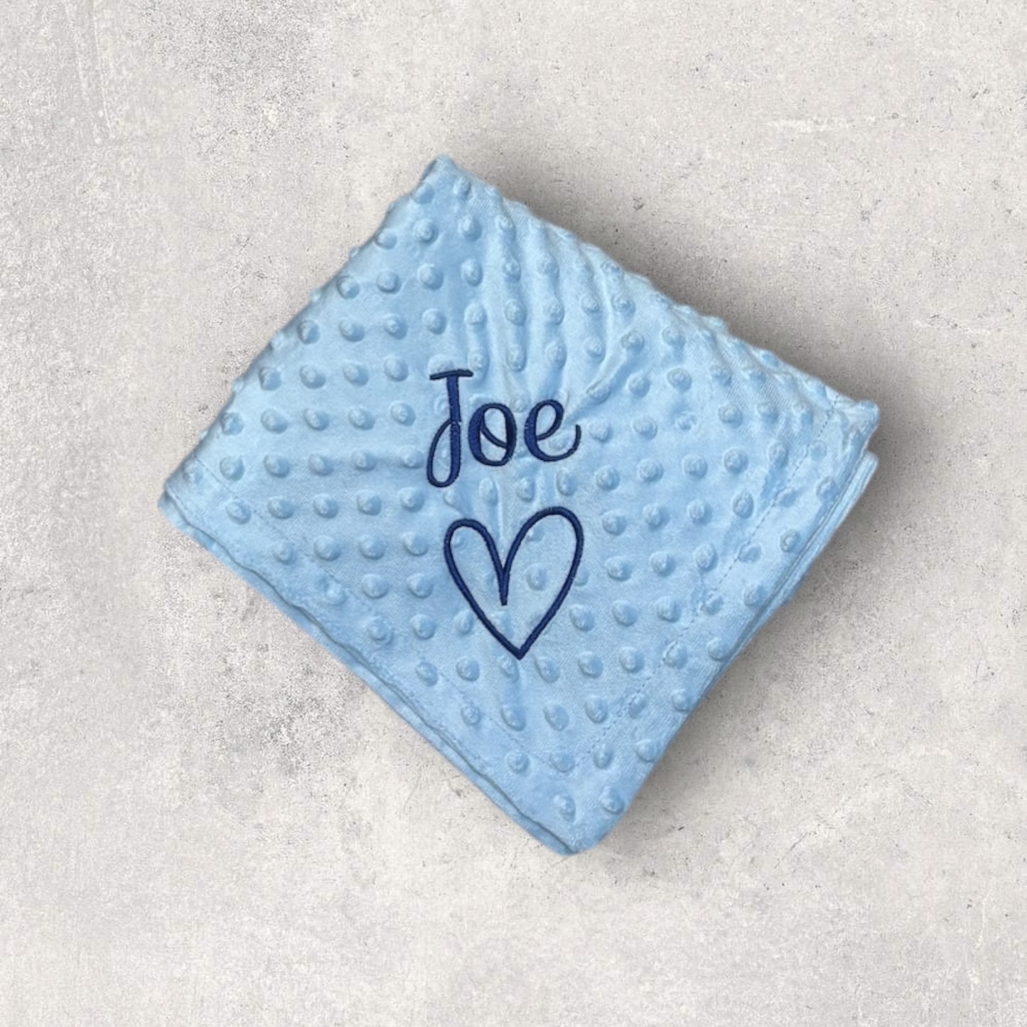 Blue textured blanket with 'Joe' and a heart on a light gray background