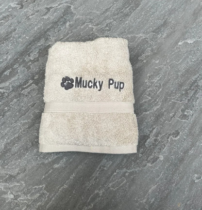 Beige towel with 'Mucky Pup' branding on a gray stone surface