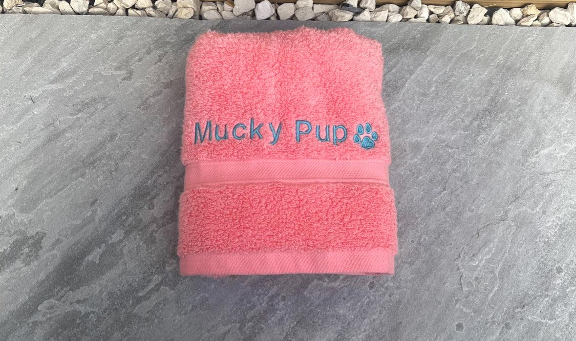 Pink towel with 'Mucky Pud' embroidery on a stone surface