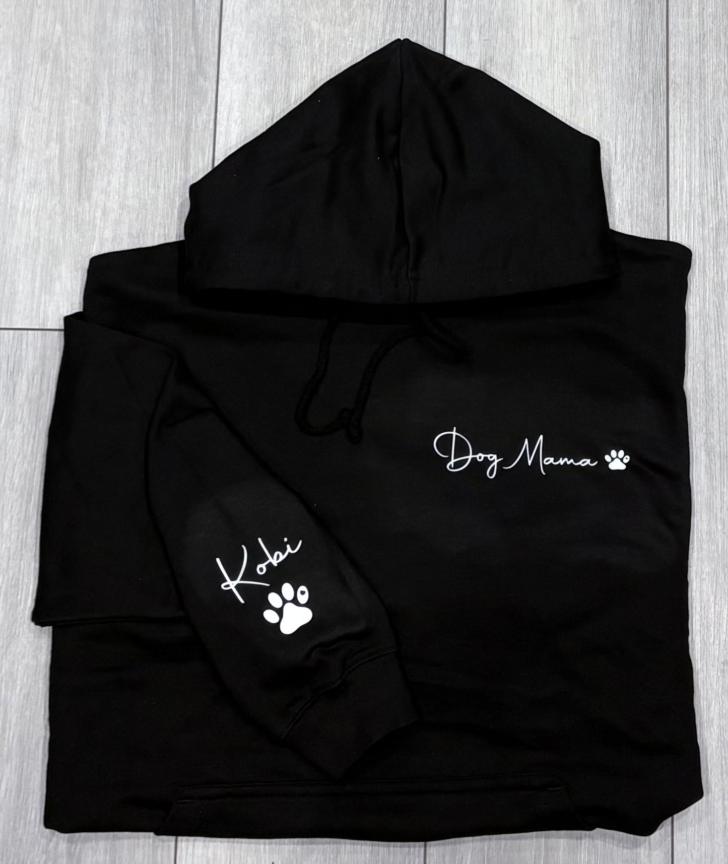 Black hoodie with 'Dog Mama' and paw print design on a wooden surface