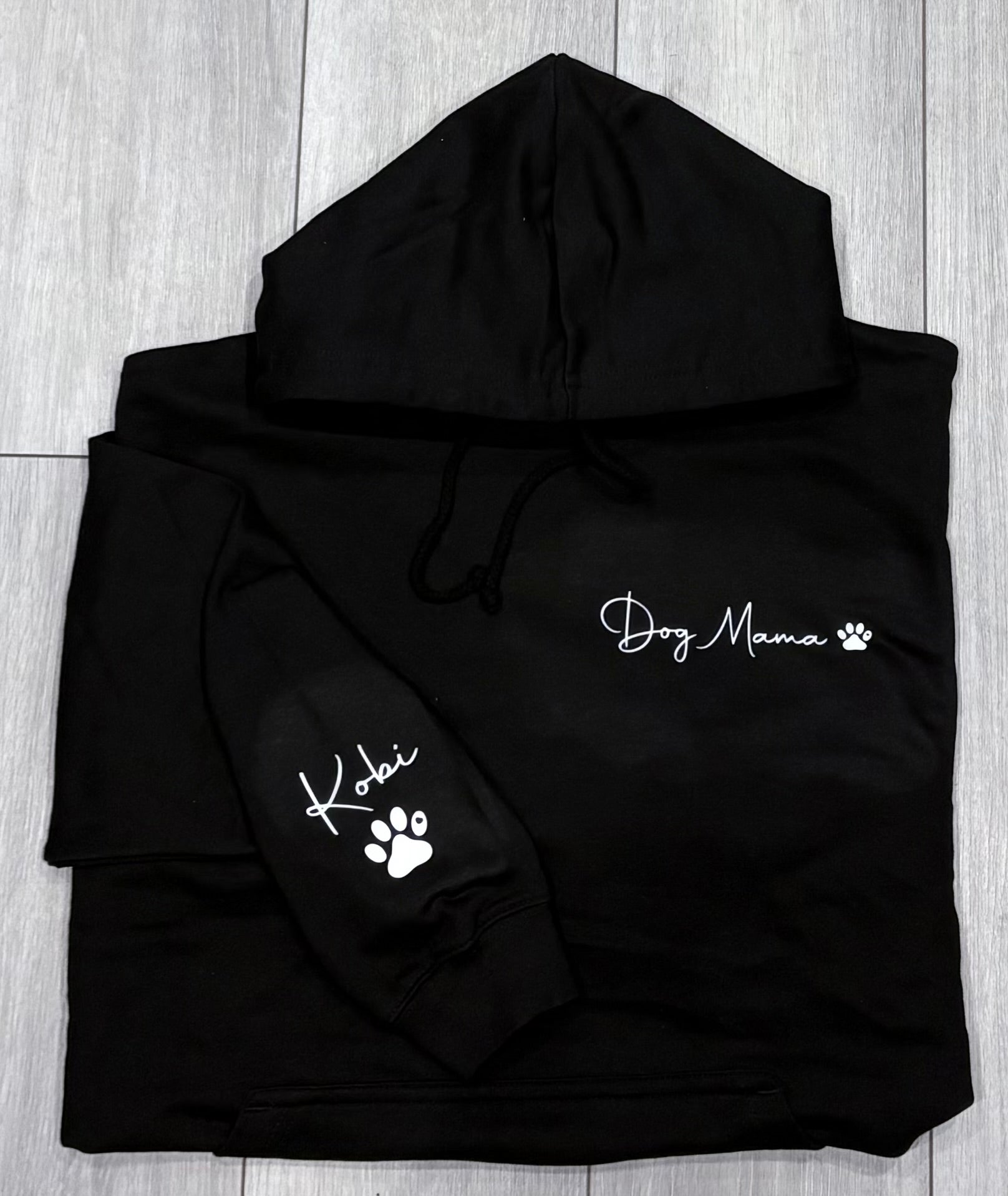 Black hoodie with 'Dog Mama' and paw print design on a wooden surface