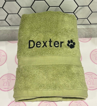 Green towel with 'Dexter' and a paw print on a tiled bathroom floor.
