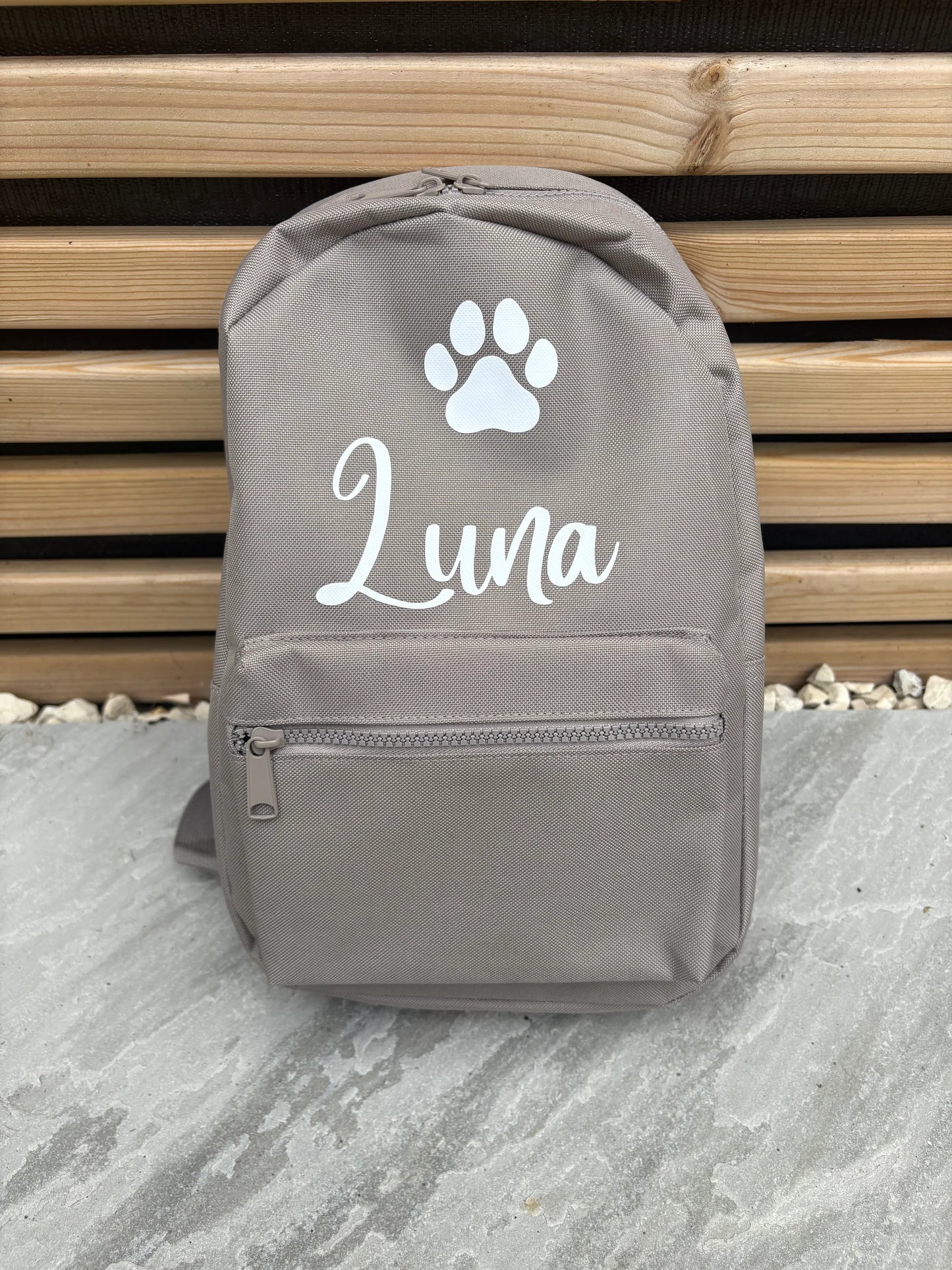 Gray backpack with a paw print and 'Luna' text on a stone surface