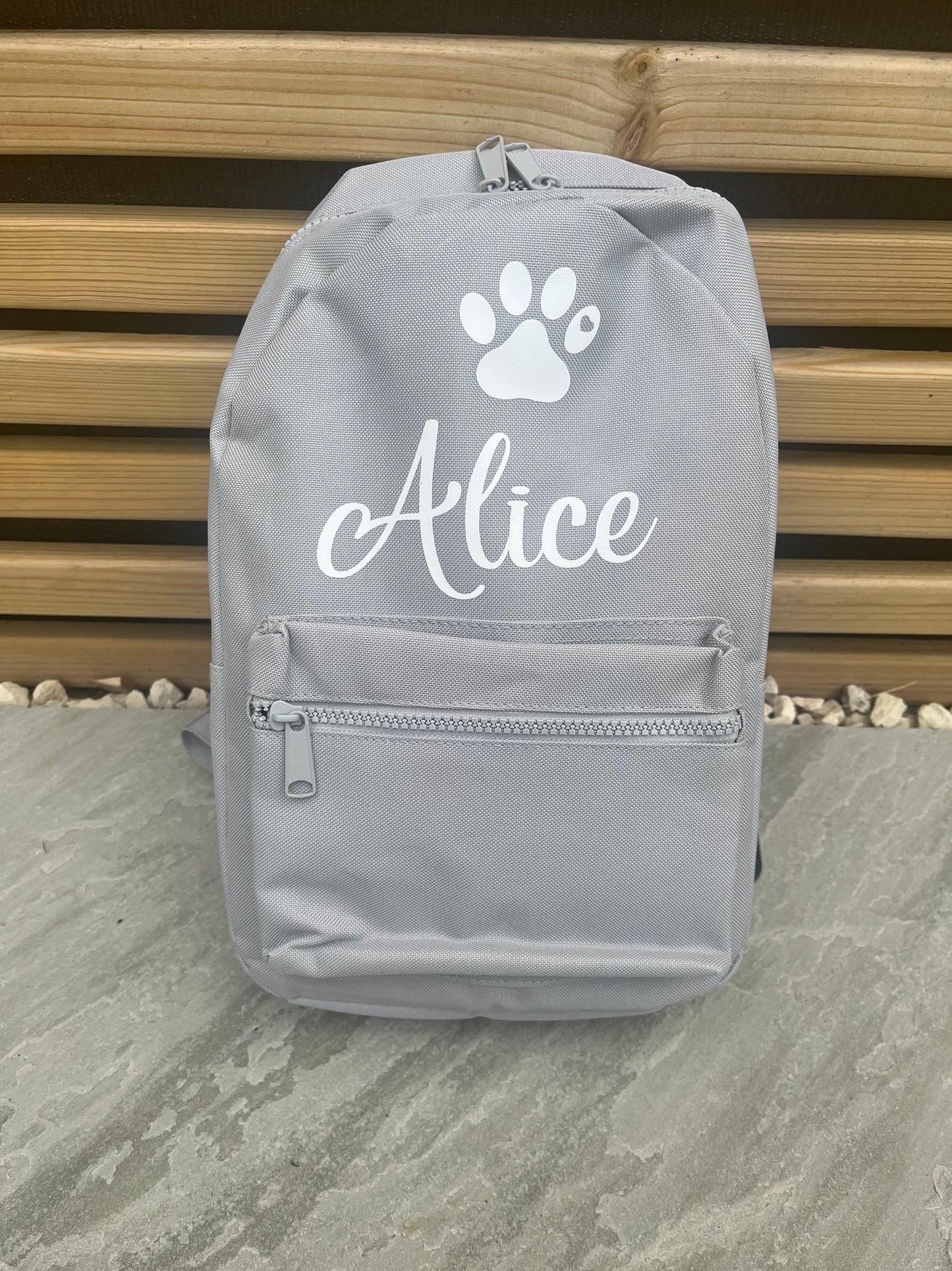 Gray backpack with 'Alice' and a paw print design on a wooden surface.
