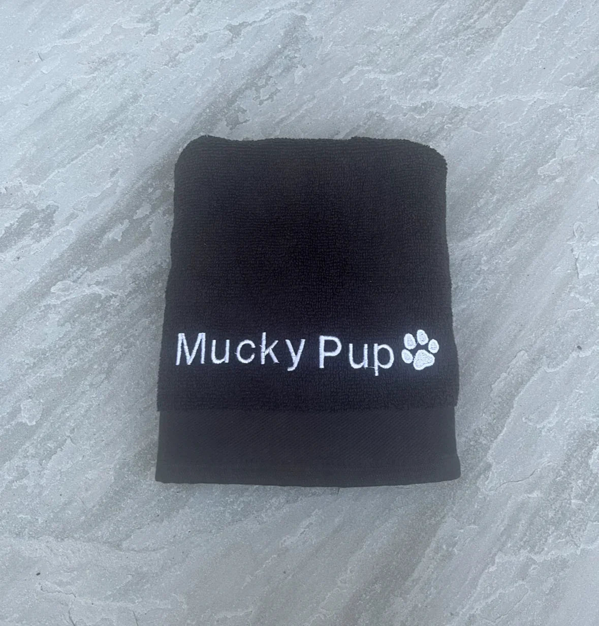 Folded black towel with 'Mucky Pup' branding on a gray surface