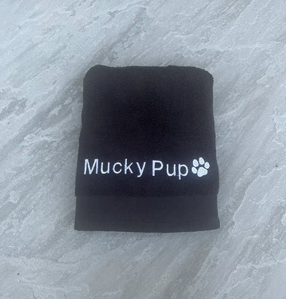 Folded black towel with 'Mucky Pup' branding on a gray surface